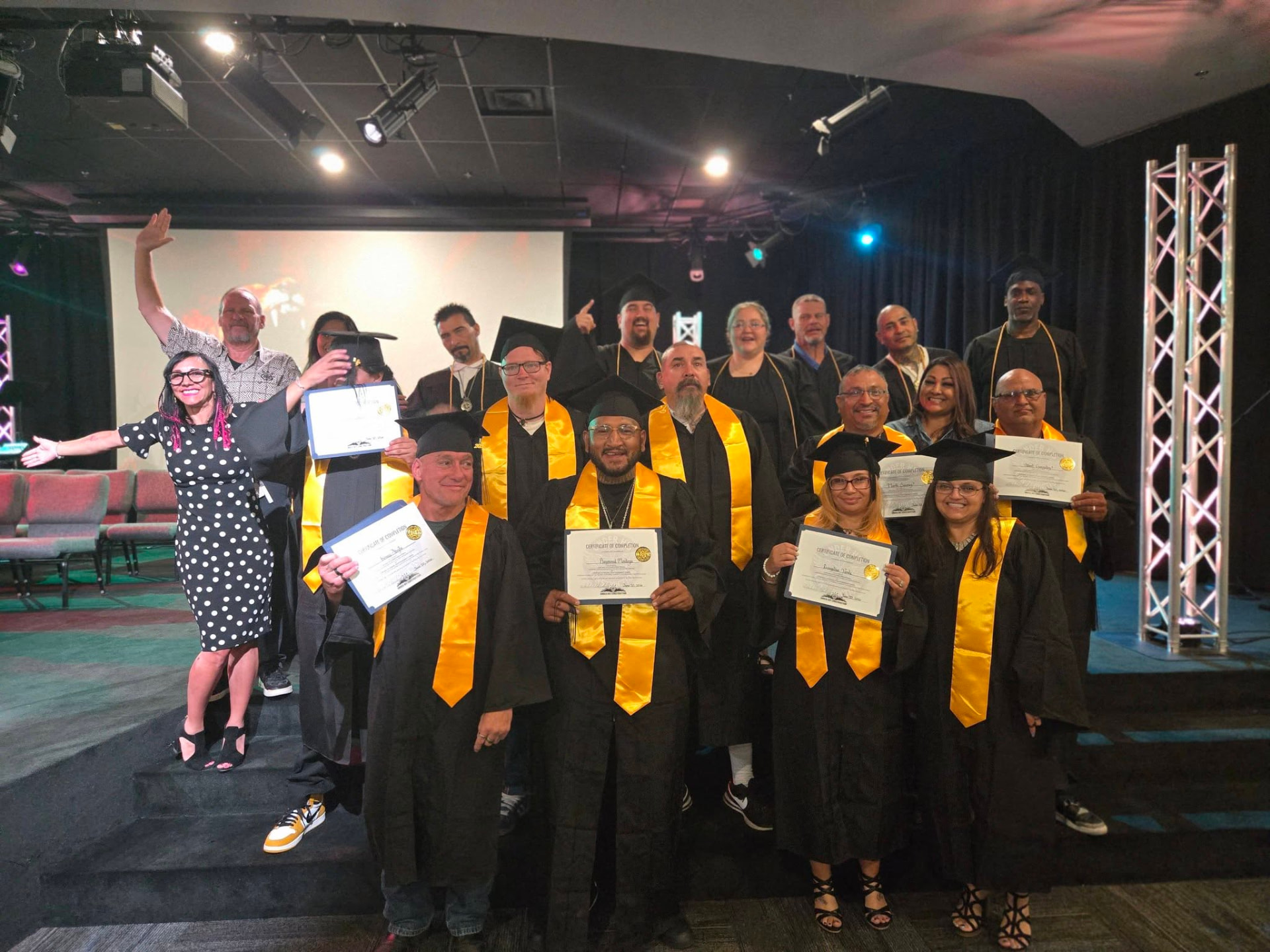 Under HIS Construction graduates in caps and gowns holding certificates of completion